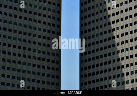 Front view of two modern high rise office towers framing a blue sky in Singapore as abstract background with strong geometry and symmetry