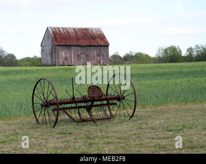 antique horse drawn cultivator with farm field and tobacco barn in background Stock Photo