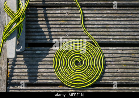 close up of a coil of green rope on a wooden deck with a metal cleat. Boat tied up on a mooring. Stock Photo