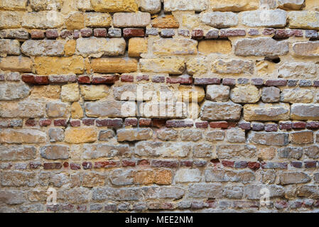 Background of irregular pattern of yellowish, red and gray grunge weathered uneven bricks stone wall surface Stock Photo