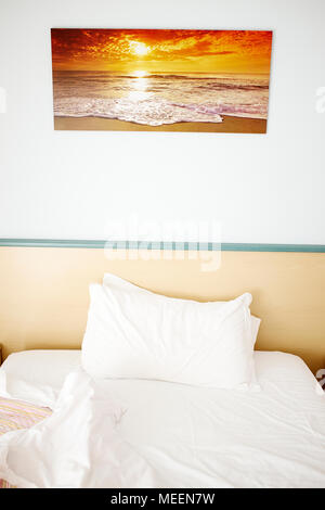 Good Morning ! - a single unmade hotel room bed with a sunset photograph on the wall above Stock Photo