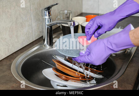 Washing dishes in the kitchen. Human hands in gloves washing the plate under running water. Stock Photo