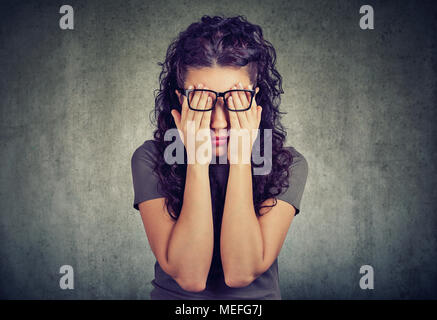 Closeup portrait young woman in glasses covering face eyes with both hands isolated on gray wall background Stock Photo