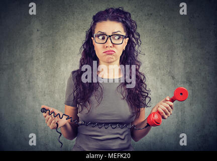 Young woman looking with bewilderment holding old fashioned red handset. Stock Photo