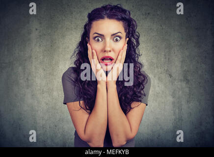 Amazed shocked woman looking at camera on gray wall background Stock Photo