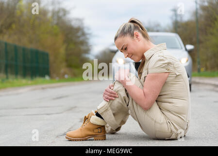 An injured young woman experiencing severe pain caused by knee sprain or fracture after car accident. Stock Photo