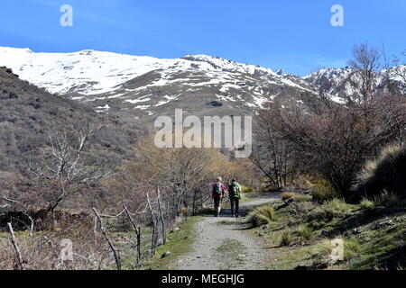 A couple hiking along the Poqueira gorge towards the snow capped Sierra Nevada mountains, Sierra Nevada, Spain