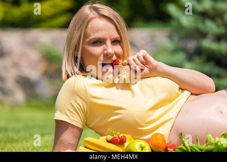 Pregnant woman lies on the grass and eats strawberries Stock Photo