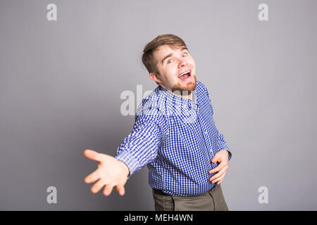 Young cheerful joyful funny man stretching hand at camera in greeting gesture, standing over gray background. Nice to meet you Stock Photo