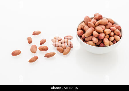 Peeled peanuts in a white ceramic cup and grains on a white table. Stock Photo