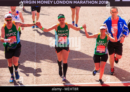 London, UK, 22nd April 2018. A trio of charity runners for the NSPCC cross the line. Runners reach the finish line on the the crowded Mall. Record numbers of runners are taking part in the famous race - just over 47,000 registered and around 41,000 have picked up their race packs at the start. Despite many struggling with the with the hot and sunny weather along the route, the race is still expected to be on track to beat previous finish line numbers, too. Credit: Imageplotter News and Sports/Alamy Live News Stock Photo