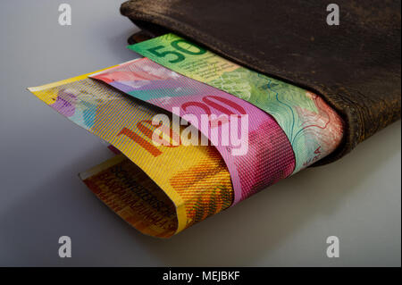 Swiss cash paper denominations - ten, twenty, fifty francs are in an old wallet. The purse with money lies on a light background. Stock Photo