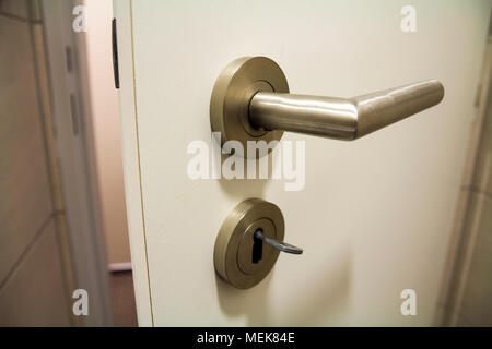 Close up of slightly open new white plastic door with bright shiny handle and keys in the lock. Safety and security of house, office. Stock Photo