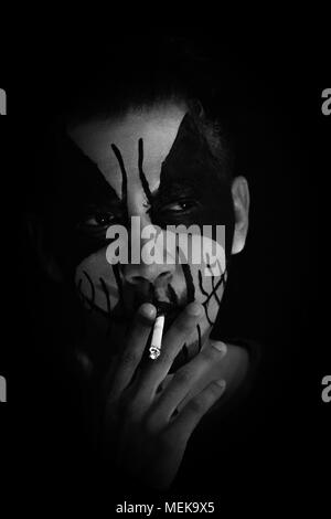 Man with the face painting was smoking with a dark black background Stock Photo