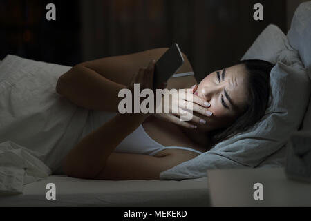 Concerned woman finding bad news in a smart phone on line in the night on the bed at home with a dark background Stock Photo