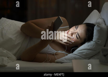 Worried woman watching bad online content in a smat phone lying on a bed in the night at home Stock Photo