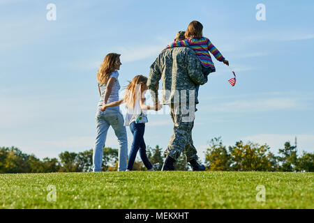 Back view soldier and his family are walking on the grass. Stock Photo