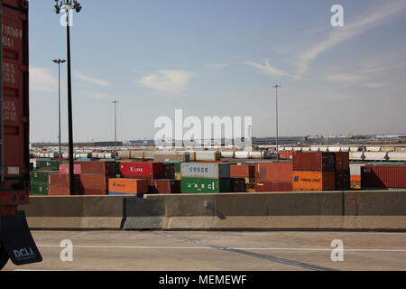 view of cargo shipping yard storage facility with a cargo box placed on a truck riding on a highway. Stock Photo
