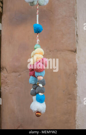 Colorful Fuzzy Balls-festive multi-colored fuzzy balls, threaded on thin rope and hanging, with a stone wall background, in Mexico Stock Photo