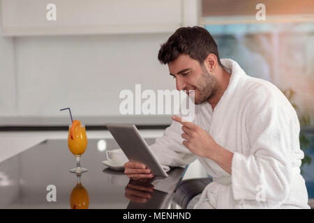 young freelancer in bathrobe working from home using tablet computer Stock Photo