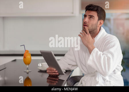 young freelancer in bathrobe working from home using tablet computer Stock Photo