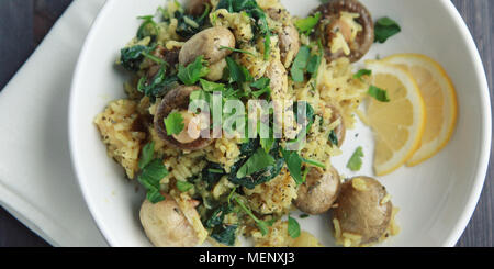 Yellow rice with mushrooms and spinach. Vegan dish. European cuisine. Vegetarian turmeric rice in the white bowl. Meatless. Wide photo. Top view. Stock Photo