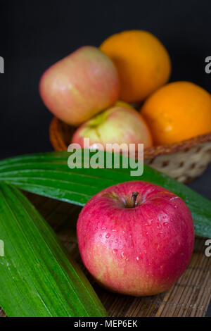 Apples with oranges on wood plate and wood basket in black space Stock Photo