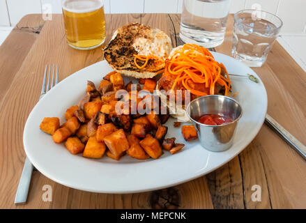 A white  fish sandwich on a roll topped with carrots strips and served with spicy diced potatoes Stock Photo