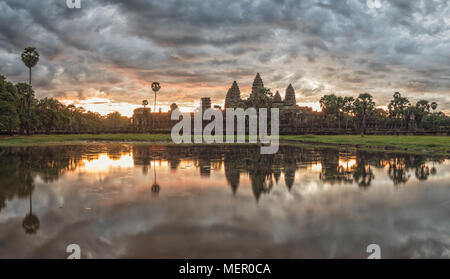 Cambodia ancient Temple Complex Angkor Wat at sunrise with dramatic clouds over the towers and reflection in the pond. Famous travel destination.