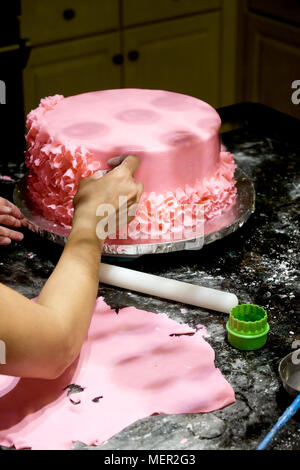 Decorating a cake pink icing flower petals are being place on home made pink icing cake by and asian female hand infront of the cake is a white roliin Stock Photo