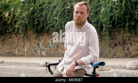 Portrait of young handsome man with beard leaning on vintage bicycle Stock Photo