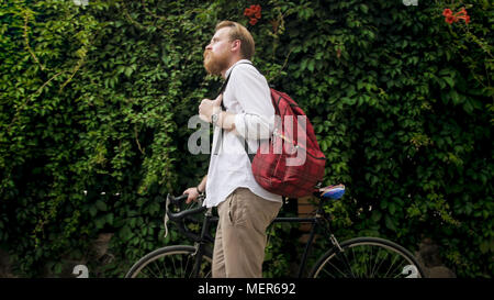 Portrait of handsome man with red backpack walking with bicycle Stock Photo