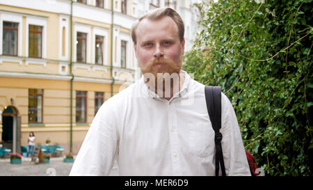 Closeup portrait of smiling young man with red beard posing on street at sun rays Stock Photo