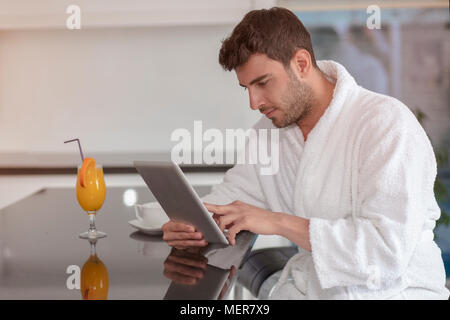 young freelancer in bathrobe working from home using tablet computer Stock Photo