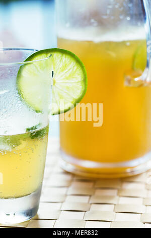 Yellow coloured drink with lime slice and jug of drink Stock Photo