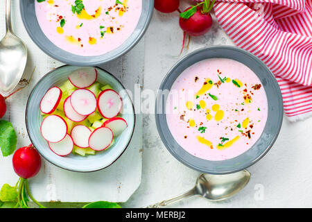 Pink cold radish soup with cucumber and yogurt garnished with dry chili, pepper, parsley, olive oil and crudites served in bowls Stock Photo