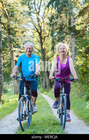 Happy and active senior couple riding bicycles outdoors Stock Photo