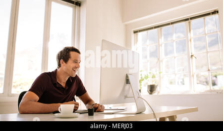 Smiling businessman working on computer and using a digitizer to make notes. Man sitting at his work table working on computer at home. Stock Photo