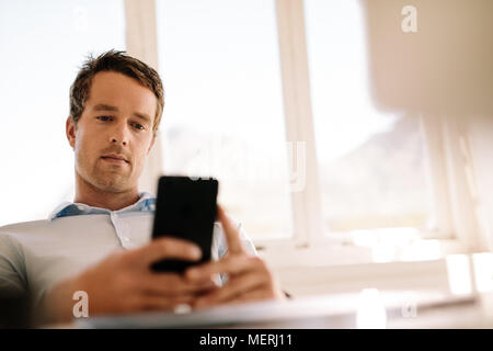 Entrepreneur working on mobile phone sitting in the comfort of home. Man operating mobile phone while relaxing at home. Stock Photo