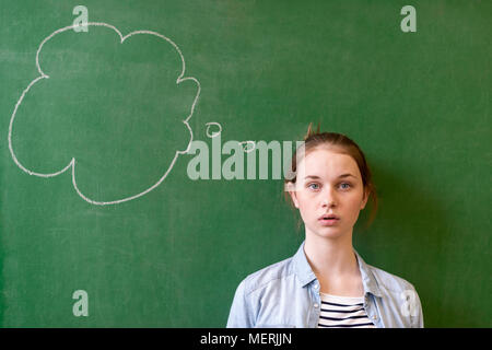 Student thinking blackboard concept. Pensive girl looking at thought bubble on chalkboard background. Caucasian student. Future, profession. Stock Photo