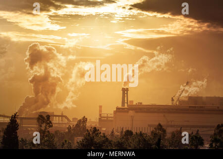 Pollution of the environment by heavy industry. Industrial landscape at sunset sky. Metallurgical plant pollutes the air. Pipes with smoke on the horizon line. Stock Photo