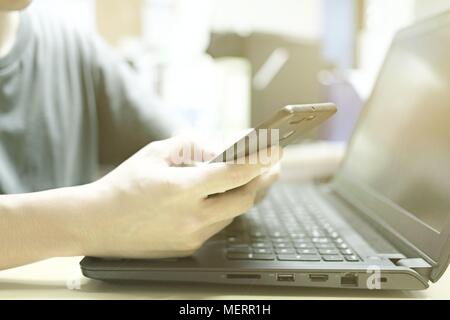 Silhouette of young man working on his laptop and using phone in his hands, Cropped image. Working Laptop Connecting Networking Concept. Stock Photo