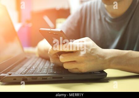Silhouette of young man working on his laptop and using phone in his hands, Cropped image. Working Laptop Connecting Networking Concept. Stock Photo