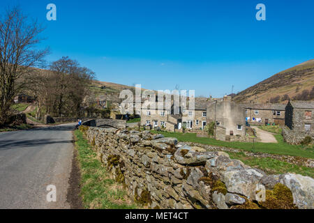 The picturesque stone houses and bridge in the village of Thwaite on a beautiful day with two walkers, Yorkshire Dales, UK Stock Photo