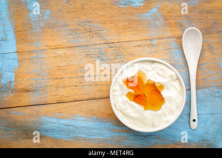 live organic Greek yogurt with natural honey in a white ceramic bowl against grunge, weathered wood, top view Stock Photo