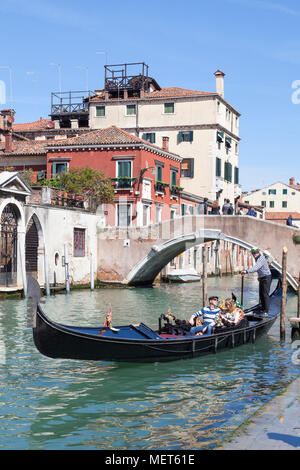 Gondolier setting off with tourists in a gondola  for a sightseeing tour below Ponte Cavallo, Cannaregio, Venice, Italy Stock Photo
