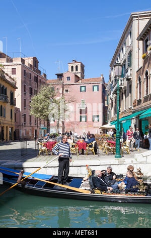 Tourists in  gondola passing through Campo Santa Maria Nova, Cannaregio, Venice, Veneto, Italy with people sitting at restaurant tables enjoying the s Stock Photo