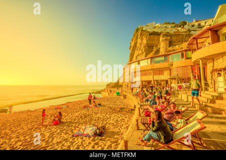 Azenhas do Mar, Portugal - August 5, 2017: tourists sunbathing and relaxing on famous beach of Azenhas do Mar in Colares, Atlantic Coast, with its natural pool visible at low tide. Sunset sunlight. Stock Photo