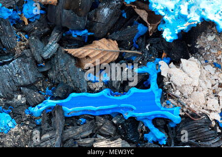 Blue melted plastic is covering a burned up garbage heap Stock Photo