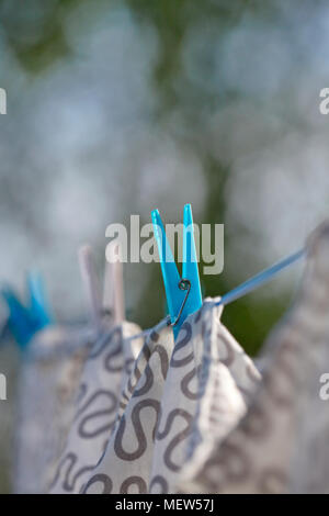 Close up of clothes pegs securing washing hanging to dry in a garden on a sunny summer day. Stock Photo